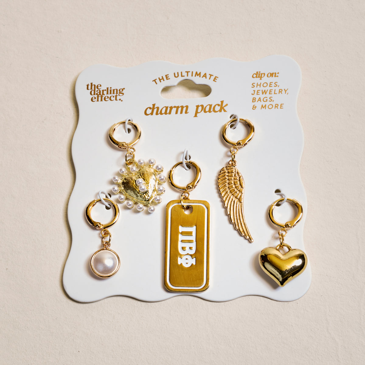 The Darling Effect’s Pi Beta Phi The Ultimate Charm Pack features five gold charms—a pearl, lion head with pearls, “IDB” tag, wing, and shiny heart—perfect for customizing shoes, bags, or creating unique sorority jewelry.