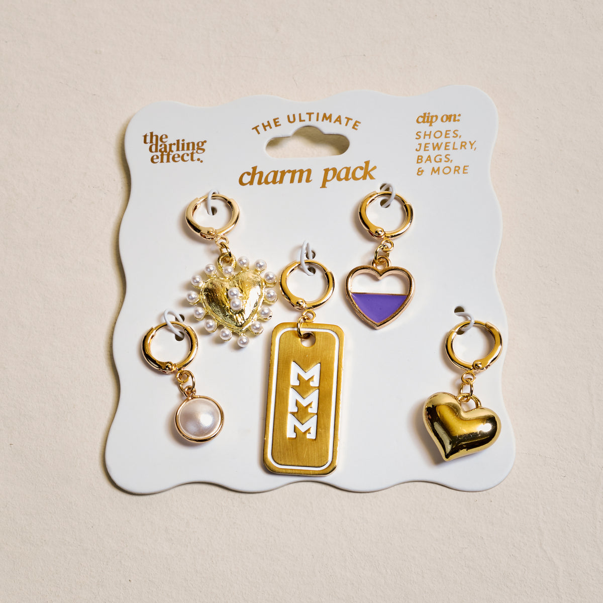 Sigma Sigma Sigma The Ultimate Charm Pack by The Darling Effect features five gold charms—pearl, lion with pearls, gold rectangle with white zigzags, purple heart, and gold heart—on a white card. Perfect for charm necklaces.