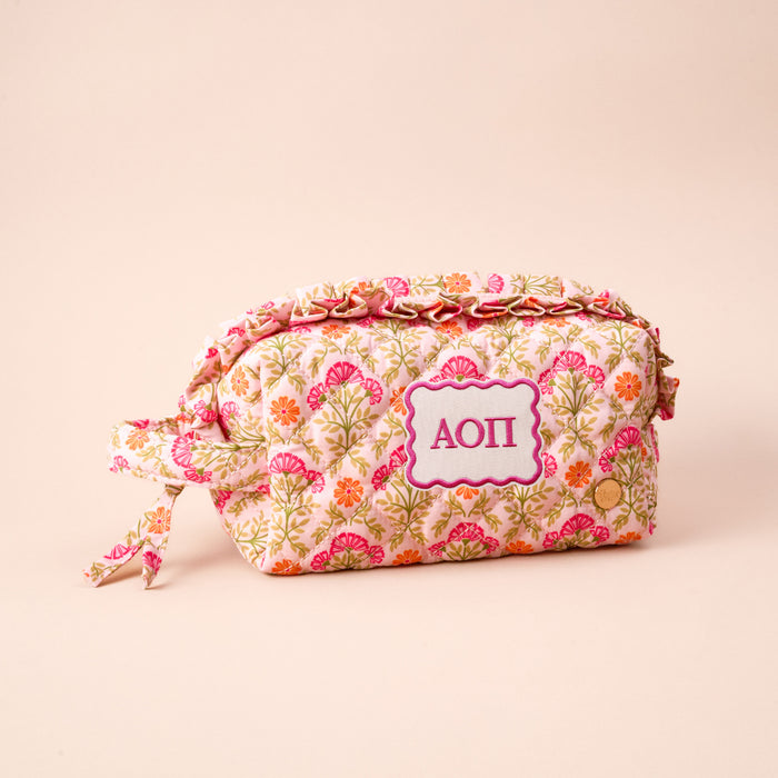 The Darling Effect Alpha Omicron Pi Essentials Quilted Cosmetic Pouch features a floral pattern, side tie, and pink and white AOII Greek letters on light beige—ideal for sorority cosmetics.