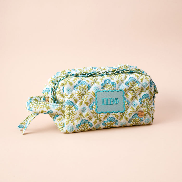 The Darling Effect's Pi Beta Phi Essentials Quilted Cosmetic Pouch features a floral design, side handle, and a turquoise embroidered ΠBΦ patch on beige—ideal for carrying your sorority necessities in style.