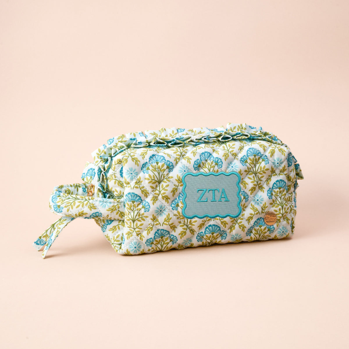 The Zeta Tau Alpha Essentials Quilted Cosmetic Pouch by The Darling Effect features a blue, green, and white floral pattern with “ZTA” embroidery, zipper closure, and a side handle—ideal for your sorority essentials.