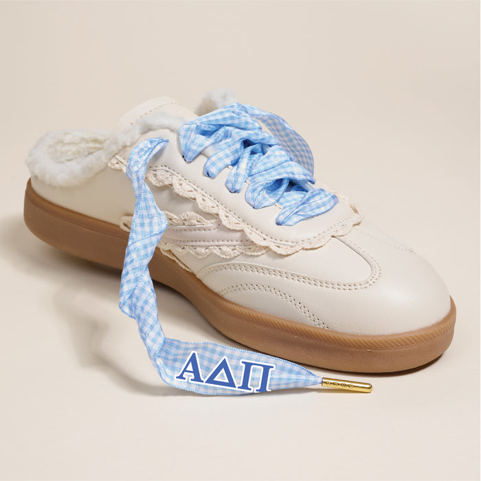 The Darling Effect’s Alpha Delta Pi Step It Up Shoelaces feature light blue gingham laces with blue ΑΔΠ Greek letters on the tips, paired with a cream sneaker, fleece lining, and a brown sole.