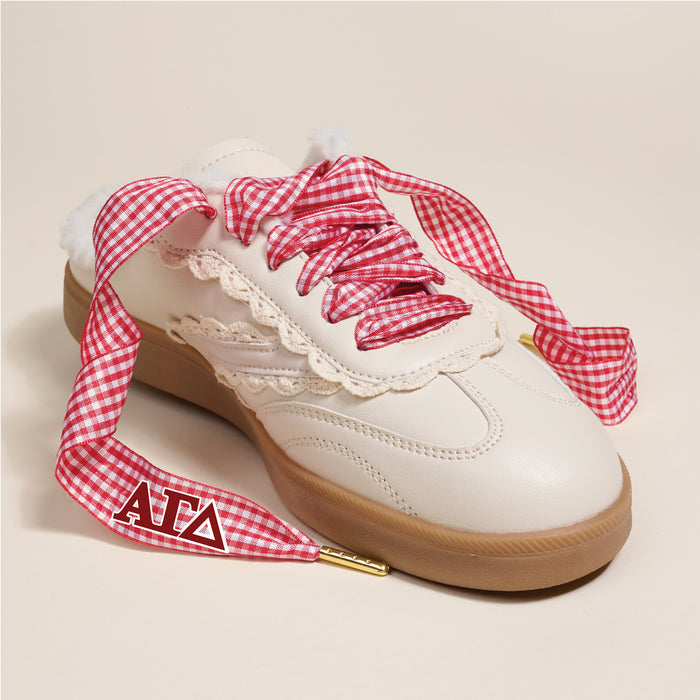 The Darling Effect’s Alpha Gamma Delta Step It Up Shoelaces, gold-tipped and printed with red ΑΓΔ letters on one tip, feature a chic red gingham print with lace trim—perfect for styling white sneakers with a tan sole.