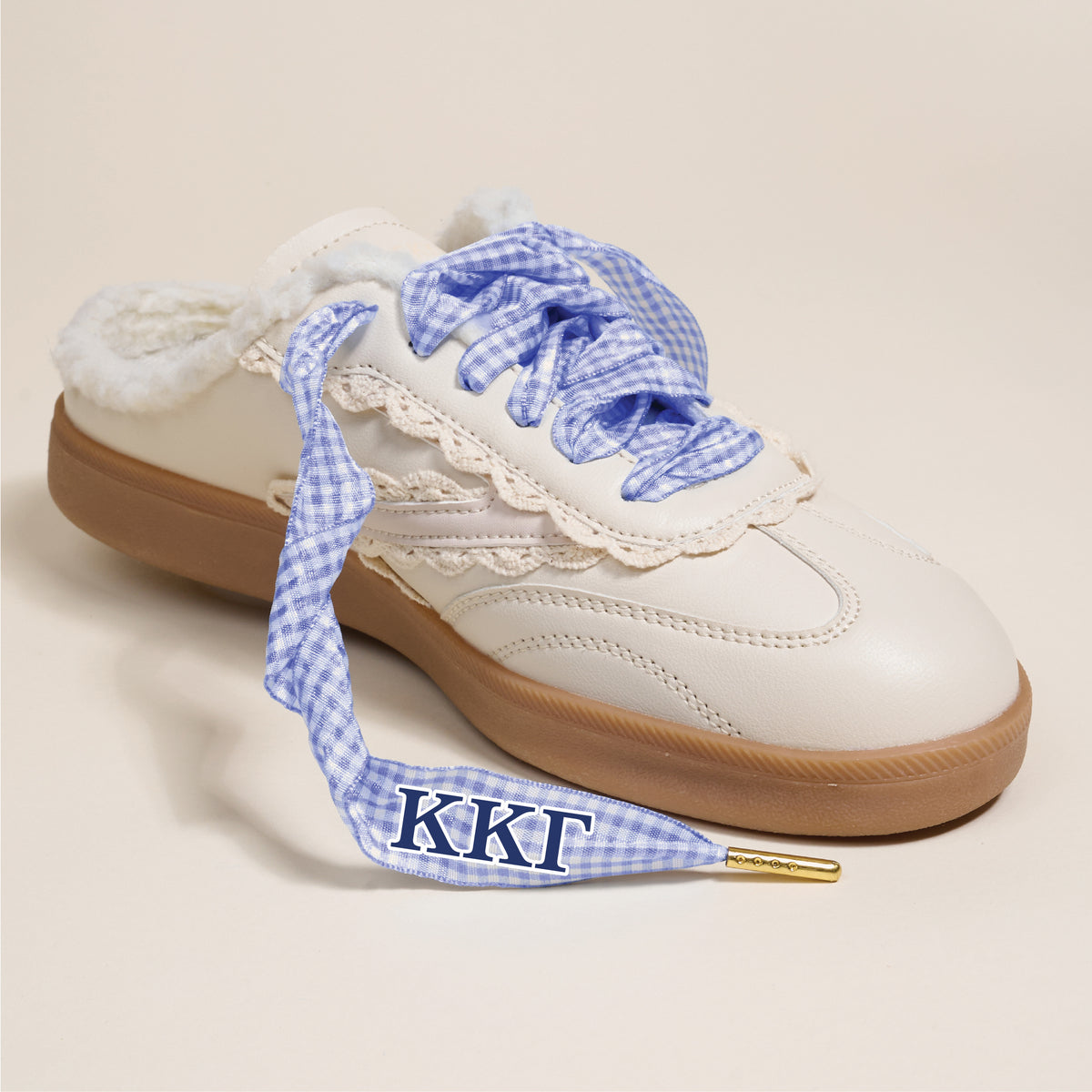 The Darling Effect’s Kappa Kappa Gamma Step It Up Shoelaces feature blue gingham print, fluffy lining, gold tips, and ΚΚΓ letters, styled on a white sneaker with a brown sole against a plain background.