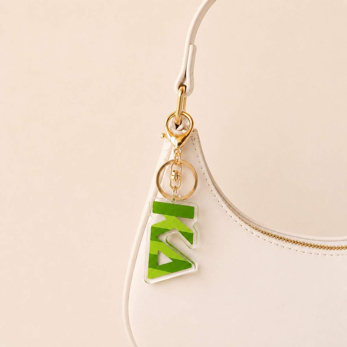 A white handbag with a gold zipper features a gold keyring and The Darling Effect's green Kappa Delta Stripes Acrylic Keychain, making it an ideal sorority or bid day gift.