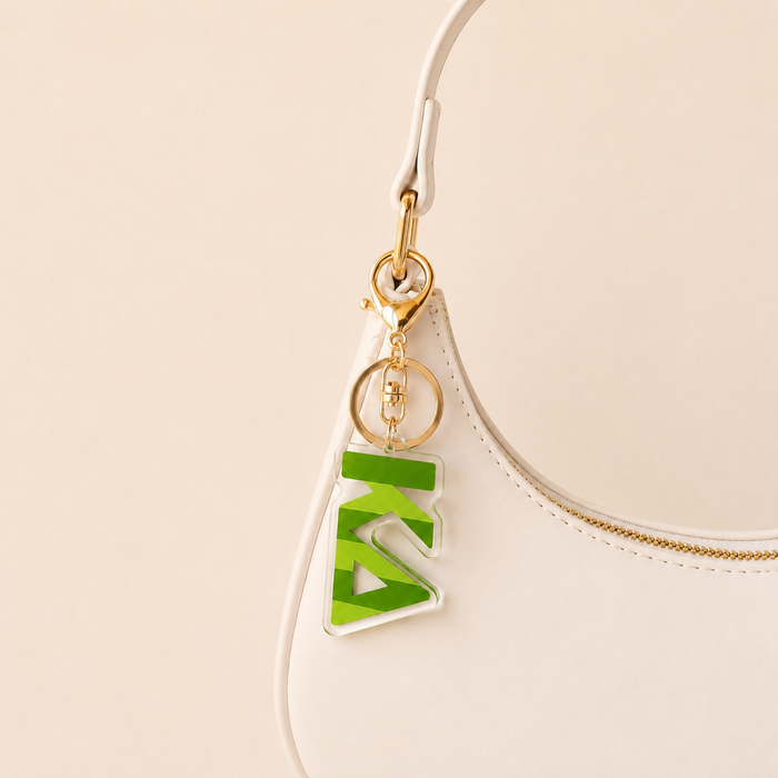 A white handbag with a gold zipper features a gold keyring and The Darling Effect's green Kappa Delta Stripes Acrylic Keychain, making it an ideal sorority or bid day gift.