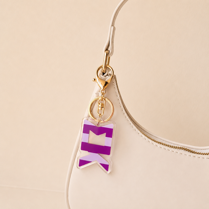 A close-up of a white handbag with a gold zipper and The Darling Effect's Sigma Kappa Stripes Acrylic Keychain, featuring bold purple and white geometric stripes—an eye-catching sorority gift.