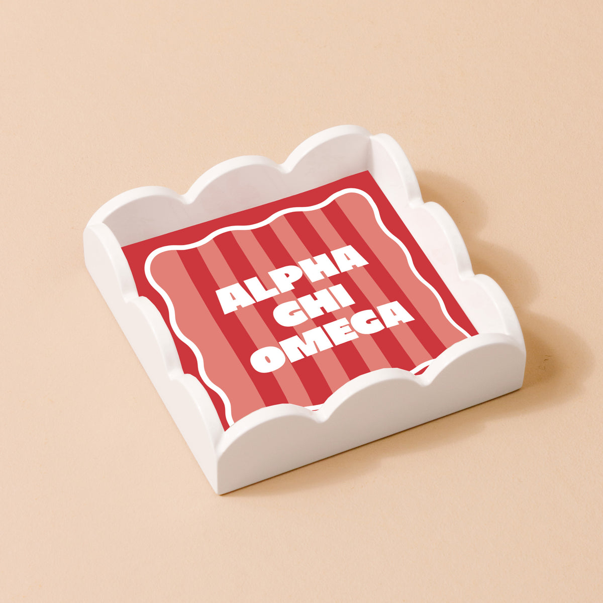 The Darling Effect’s Alpha Chi Omega Scallop Trinket Tray is a square, white tray with scalloped edges and a red and pink striped insert that reads “ALPHA CHI OMEGA”—perfect for holding jewelry or keepsakes.