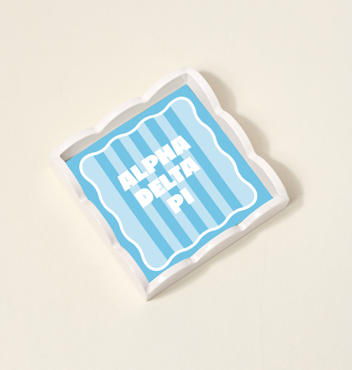 The Darling Effect Alpha Delta Pi Scallop Trinket Tray features a square shape with blue and light blue vertical stripes and bold white ALPHA DELTA PI text, perfect as a stylish jewelry organizer or accessory tray.