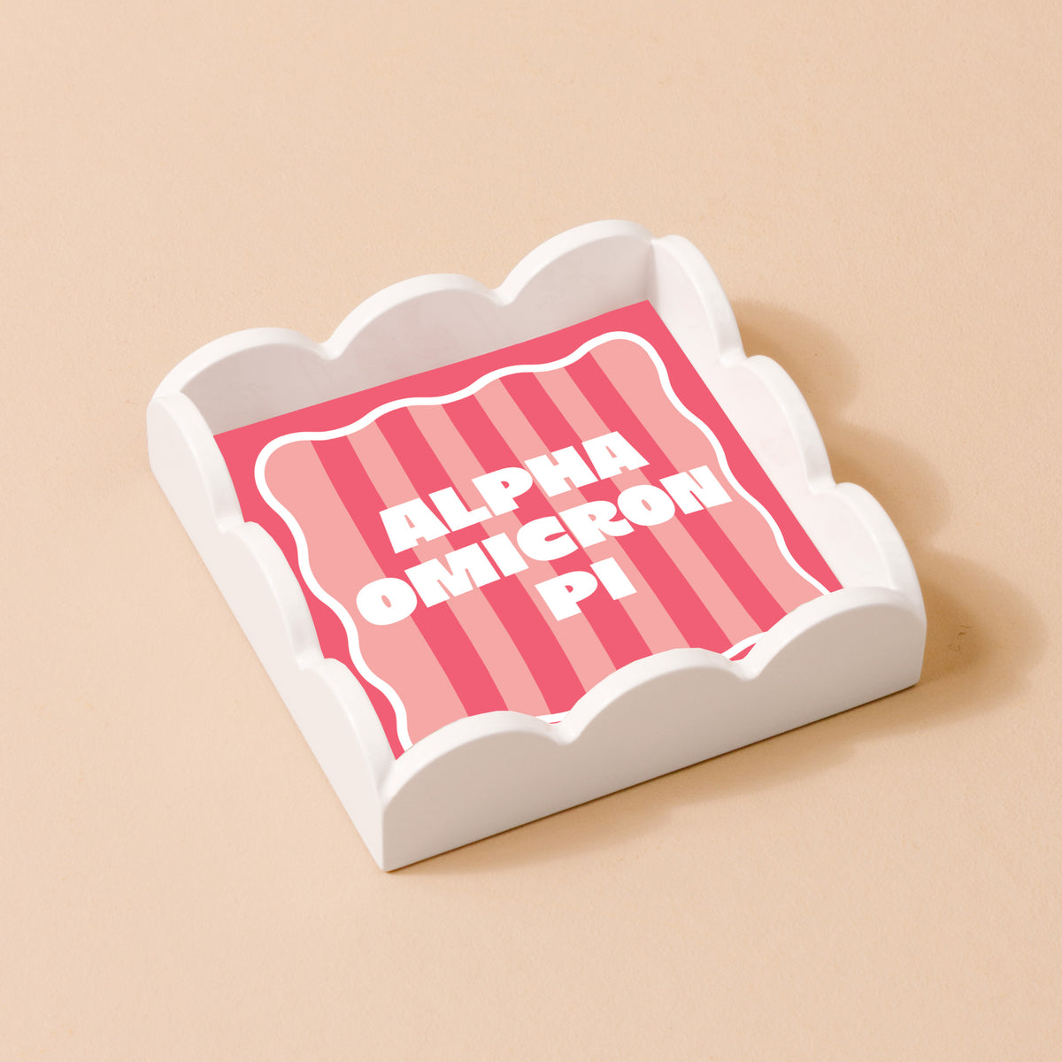The Darling Effect Alpha Omicron Pi Scallop Trinket Tray features a white finish with a pink and red striped base and bold white lettering—ideal as an accessory tray or jewelry organizer.