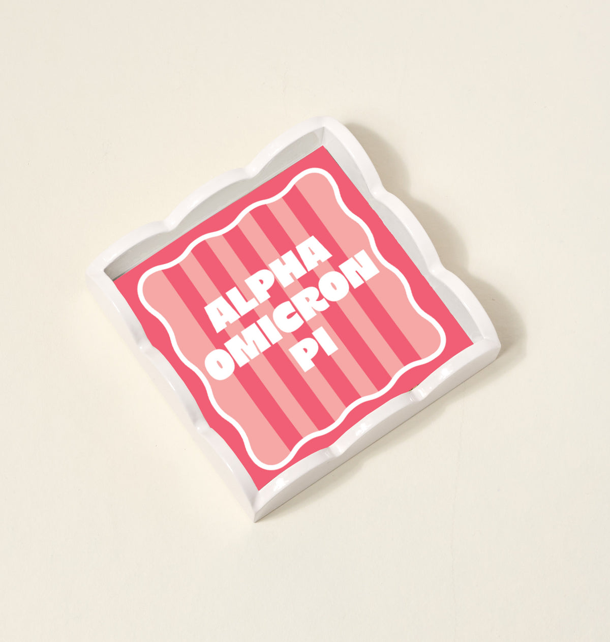 The Darling Effect's Alpha Omicron Pi Scallop Trinket Tray is a square, wavy-edged organizer with pink stripes and bold white ALPHA OMICRON PI text—ideal for jewelry or accessories.