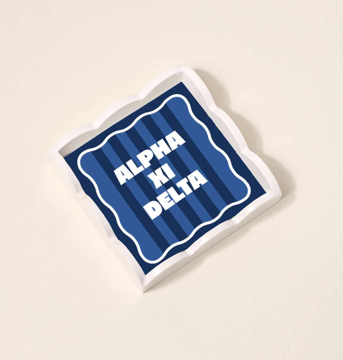 The Darling Effect's Alpha Xi Delta Scallop Trinket Tray features a blue striped design with bold white ALPHA XI DELTA lettering—ideal as a stylish vanity tray or jewelry organizer.