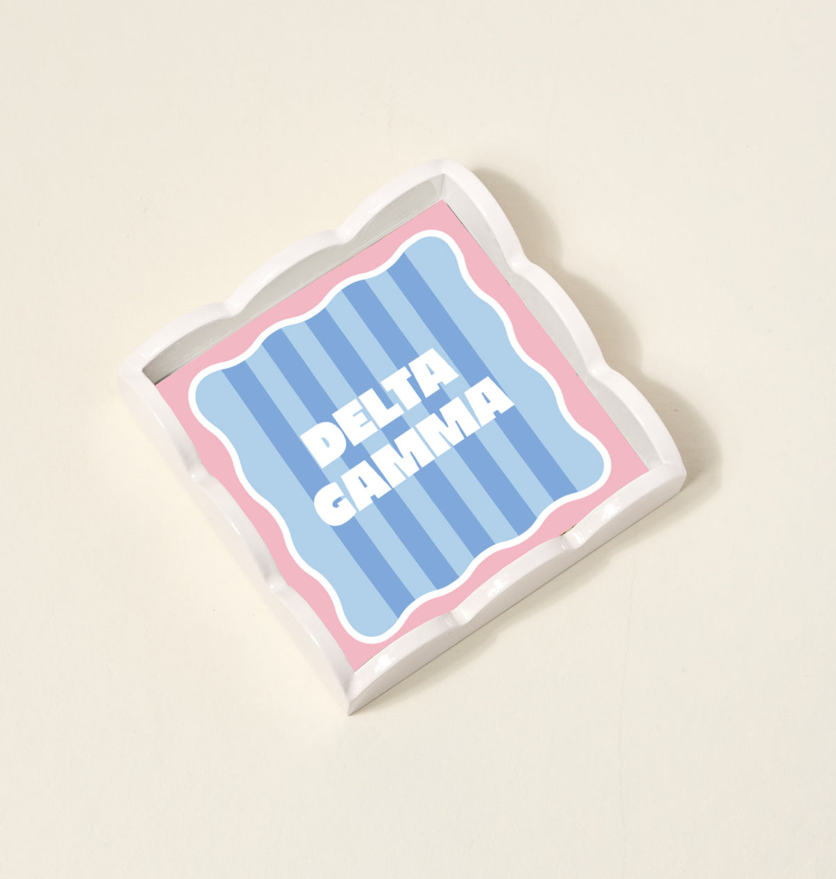 The Darling Effect Delta Gamma Scallop Trinket Tray features blue stripes, a pink border, and wavy edges with bold white DELTA GAMMA lettering—ideal as a jewelry organizer or accessory tray.