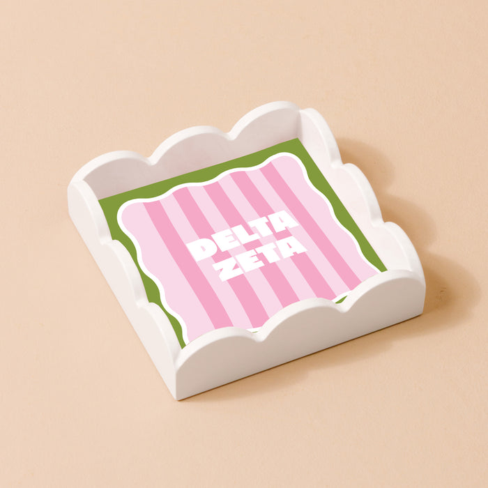 The Darling Effect's Delta Zeta Scallop Trinket Tray features a pink and green striped insert with bold white "DELTA ZETA" lettering, ideal as a vanity tray or jewelry organizer.