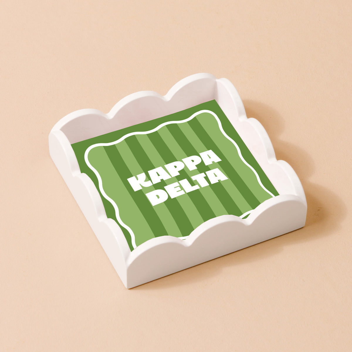 The Darling Effect’s Kappa Delta Scallop Trinket Tray features white scalloped edges and a green striped square with bold white Kappa Delta letters—ideal as a jewelry organizer or accessory tray.
