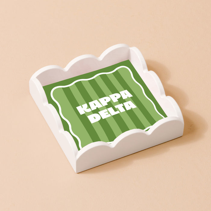 The Darling Effect’s Kappa Delta Scallop Trinket Tray features white scalloped edges and a green striped square with bold white Kappa Delta letters—ideal as a jewelry organizer or accessory tray.