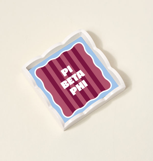 The Darling Effect’s Pi Beta Phi Scallop Trinket Tray has wavy edges, bold white PI BETA PHI lettering on maroon, and a light blue border—ideal as an accessory tray on any light surface.
