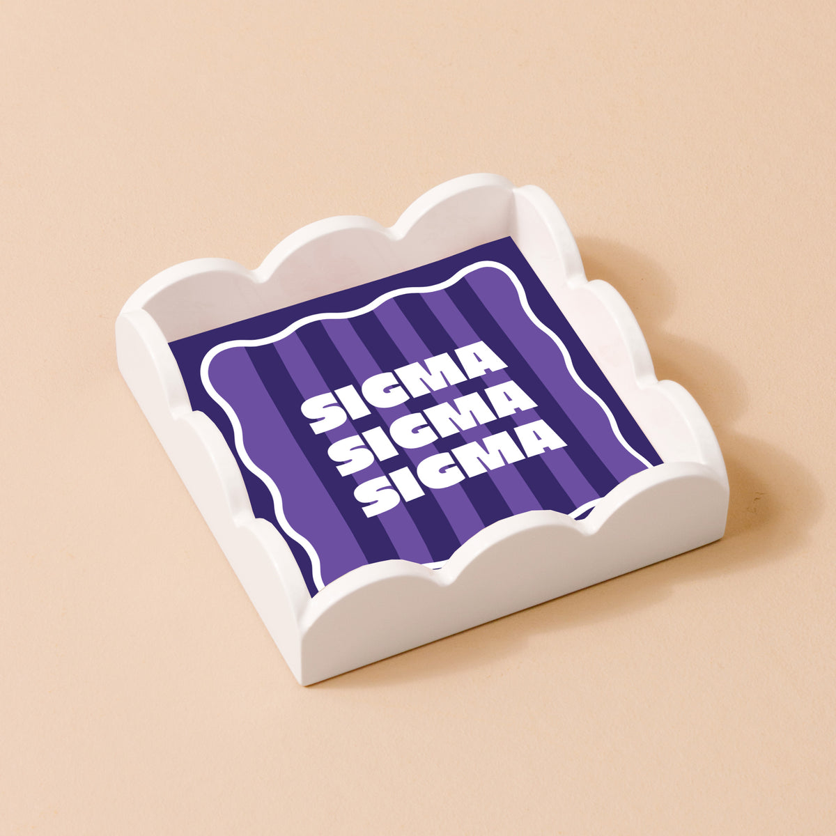 The Darling Effect's Sigma Sigma Sigma Scallop Trinket Tray features a scalloped white edge and holds a square card with “SIGMA” repeated three times on a purple striped background—ideal as an accessory or jewelry organizer.