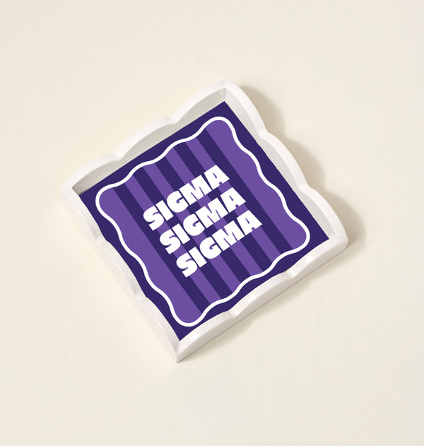 The Darling Effect’s Sigma Sigma Sigma Scallop Trinket Tray features bold white Greek letters on a purple striped background with wavy edges—perfect for organizing jewelry and adding sorority style to any space.