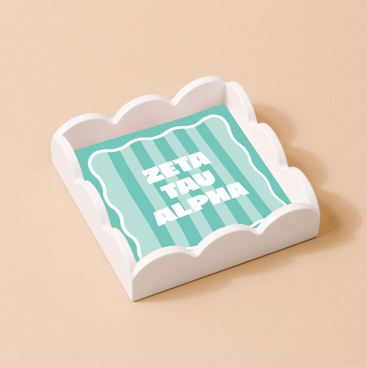 The Darling Effect's Zeta Tau Alpha Scallop Trinket Tray features a white scallop design with a mint green and white striped base and bold white ZETA TAU ALPHA letters, ideal as an accessory or jewelry organizer against a beige background.