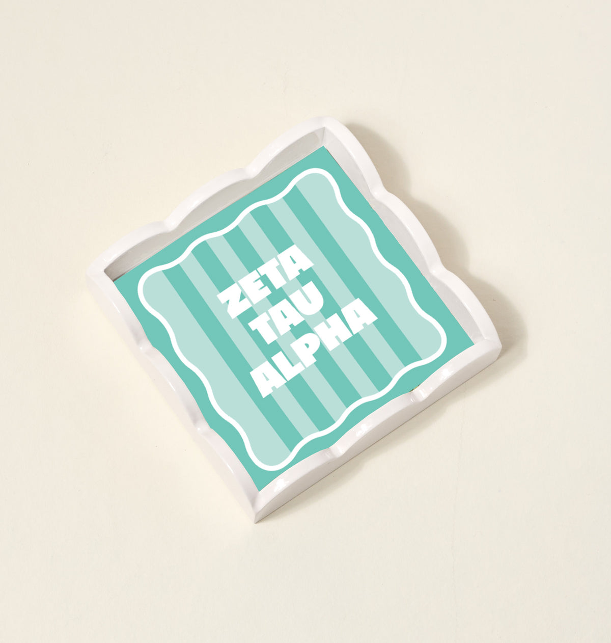 The Darling Effect’s Zeta Tau Alpha Scallop Trinket Tray features scalloped white edges, a teal striped interior, and bold white “ZETA TAU ALPHA” text—perfect as a stylish accessory tray for any space.