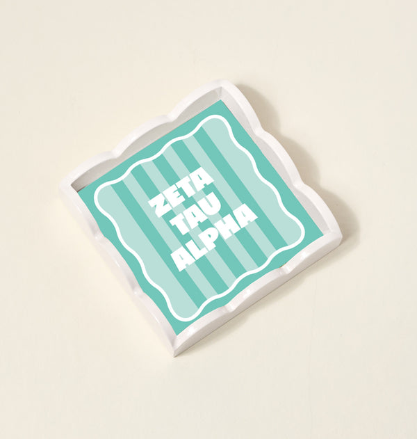 The Darling Effect’s Zeta Tau Alpha Scallop Trinket Tray features scalloped white edges, a teal striped interior, and bold white “ZETA TAU ALPHA” text—perfect as a stylish accessory tray for any space.