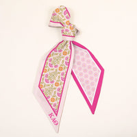 The Darling Effect’s Kappa Alpha Theta Twirl & Tie Scarf Accessory features pink, yellow, and green florals on one side, a pink geometric print on the other, and ΚΑΘ Greek letters in the corner—perfect for adding boutique charm.