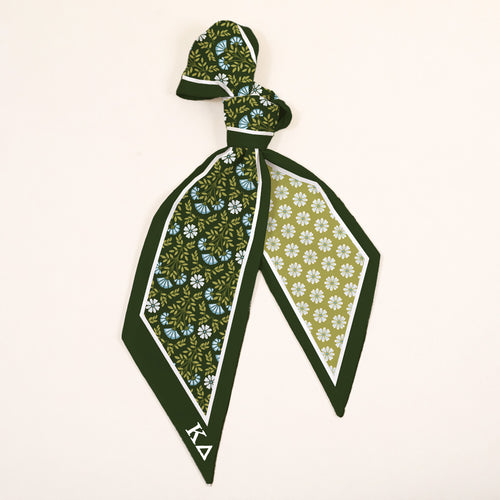 The Darling Effect's Kappa Delta Twirl & Tie Scarf Accessory features Greek letters ΚΔ, a floral pattern of blue, yellow, and white blooms, and a light green silk background—perfect for sorority style.