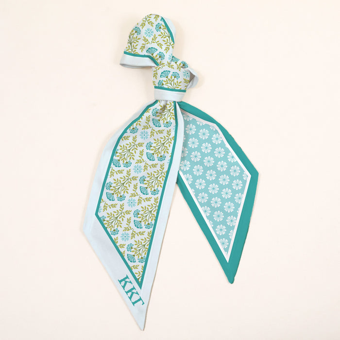The Darling Effect’s Kappa Kappa Gamma Twirl & Tie Scarf Accessory features blue and green floral and geometric patterns, light blue edges, a KKG monogram, and instantly adds boutique charm to your look.