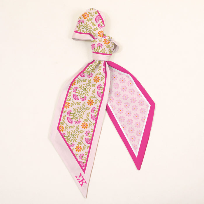 The Darling Effect's Sigma Kappa Twirl & Tie Scarf Accessory features pink, yellow, and green floral print on one side, a pink geometric pattern on the other, and bright pink edging—perfect for versatile styling on a cream background.