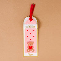 The Darling Effect’s Teddy Bear Hugs Acrylic Bookmark features a teddy bear with a heart, red accents, and a velvet ribbon tassel—a sweet romantic gift for someone special.