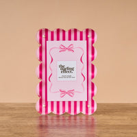 The Darling Effect’s Sweetheart Stripes Rectangle Scalloped Acrylic Frame, with pink and white vertical stripes and stylish scalloped edges, adds charm to any space.