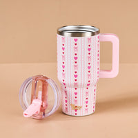The Darling Effect’s Oh So Lovely 20 oz Lifestyle Flip Straw Tumbler is an insulated stainless steel mug with a pink handle, heart and bow design, and a matching transparent pink lid, shown on a beige background.
