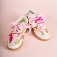 The Darling Effect’s Velvet Crush Dazzle Shoe Charm Pack adds pink gingham, velvet bows, gold chains, and cute charms to cream and gold sneakers with gum soles—styled on a pastel pink background for Valentine’s flair.