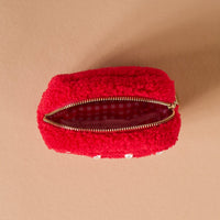 The Darling Effect's Square Pearl Red Teddy Pouch is a small, fuzzy sherpa pouch with pearls, a gold zipper, and a red and white gingham-lined interior, shown from above on a tan surface.