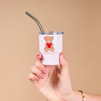 A hand holds The Darling Effect's Teddy Bear Hugs 2 oz Tiny Tumbler, featuring a cartoon bear with a red heart and a metal straw in the pink cup—an adorable Valentine’s gift.
