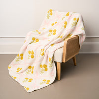 The Marigold Lane Pink Cozy Dreams Luxe Blanket by the-darling-effect, featuring yellow floral and pale pink geometric designs, is draped over a wooden chair, its ultra-soft polyester microfiber fabric adding cozy warmth to the scene.