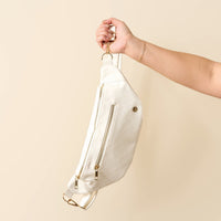 A hand displays The Darling Effect’s White Trendy Luxe Belt Bag in quilted vegan leather with gold zippers against a cream background—offering stylish, hands-free convenience.