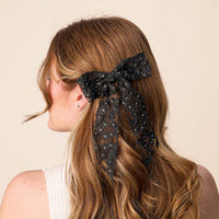 A woman's back is shown with wavy auburn hair pulled back by the-darling-effect's Black Ditzy Daisies Hair Bow, featuring delicate floral details and a gold barrette clip for an elegant finish.
