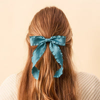 A person with long, wavy light brown hair, seen from behind, wears The Darling Effect's Dark Teal Ruffle Hair Bow and a cream knit sweater against a plain beige background.