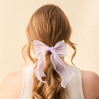 Back view of a woman with long, wavy auburn hair styled with the-darling-effect's Lilac Sheer Pearl Hair Bow, adorned with small white pearls.