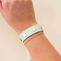 The Darling Effect's Aqua Woven Stacker Bracelet, featuring gold flower details, is styled on the wrist with a delicate gold chain bracelet for a perfect floral stacker look.