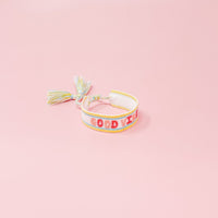 The Darling Effect's Good Vibes Woven Bracelet features pastel embroidery and playful tassels, with "GOOD VIBES" in pink and orange lettering.