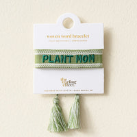 The Darling Effect’s Plant Mom Woven Bracelet is a green bracelet with “PLANT MOM” embroidered in teal, tassel ends, and comes on a white card. It’s part of their Adjustable Woven Word Bracelets collection.