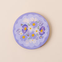 The-darling-effect’s Bouquet Beauty Purple Wood Enamel Coaster features white daisies, yellow centers, and purple pansies on a periwinkle background with scalloped edges—a stylish and durable decorative piece.