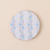The-darling-effect’s Petal Parade Blue Wood Enamel Coaster features blue and purple floral designs with green leaves on white and light blue stripes—a stylish, durable addition to your coaster collection.