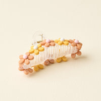 The Peachy Daisy Claw Clip by The Darling Effect is a transparent hair accessory featuring pastel flower designs in yellow, pink, white, and beige, shown on a light cream background.