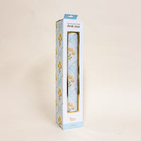 The Marigold Lane Blue Style Station Desk Mat by the-darling-effect features a floral design with yellow flowers and blue bows. Its white packaging displays matching yellow blooms, making it a charming workspace accessory.