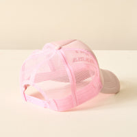 The Darling Effect Girl Mama Trckr Hat, a light pink mesh trucker style from our trendy hat collection, is displayed from the back on a white surface against a neutral beige background.