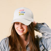 A smiling woman wears the-darling-effect's Have a Nice Day Trucker Hat, featuring colorful retro script embroidery, paired with a denim jacket.